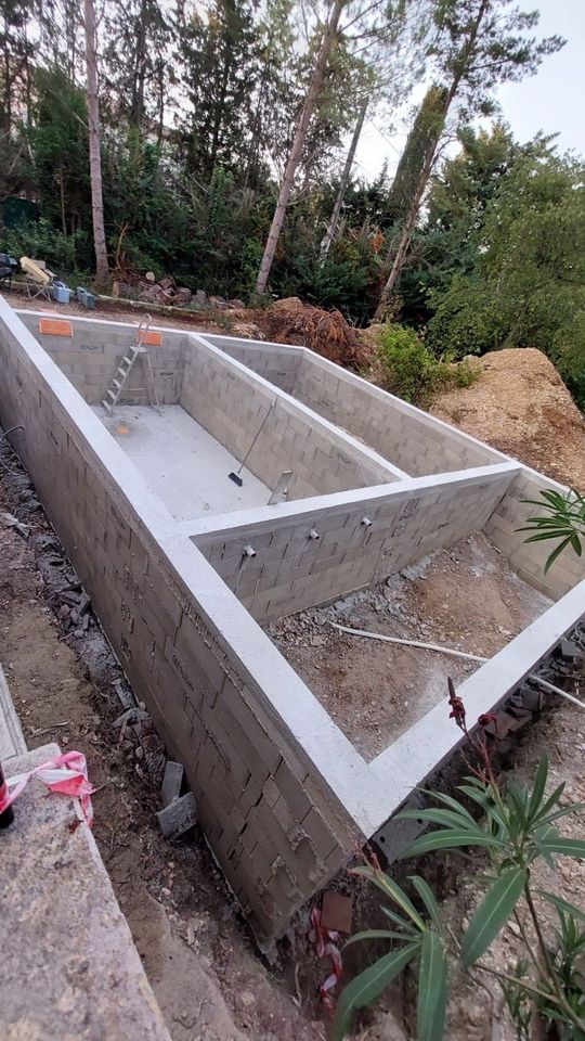 Piscine en béton en construction, à l'extérieur ; entourée de terre, de verdure et d'arbres.