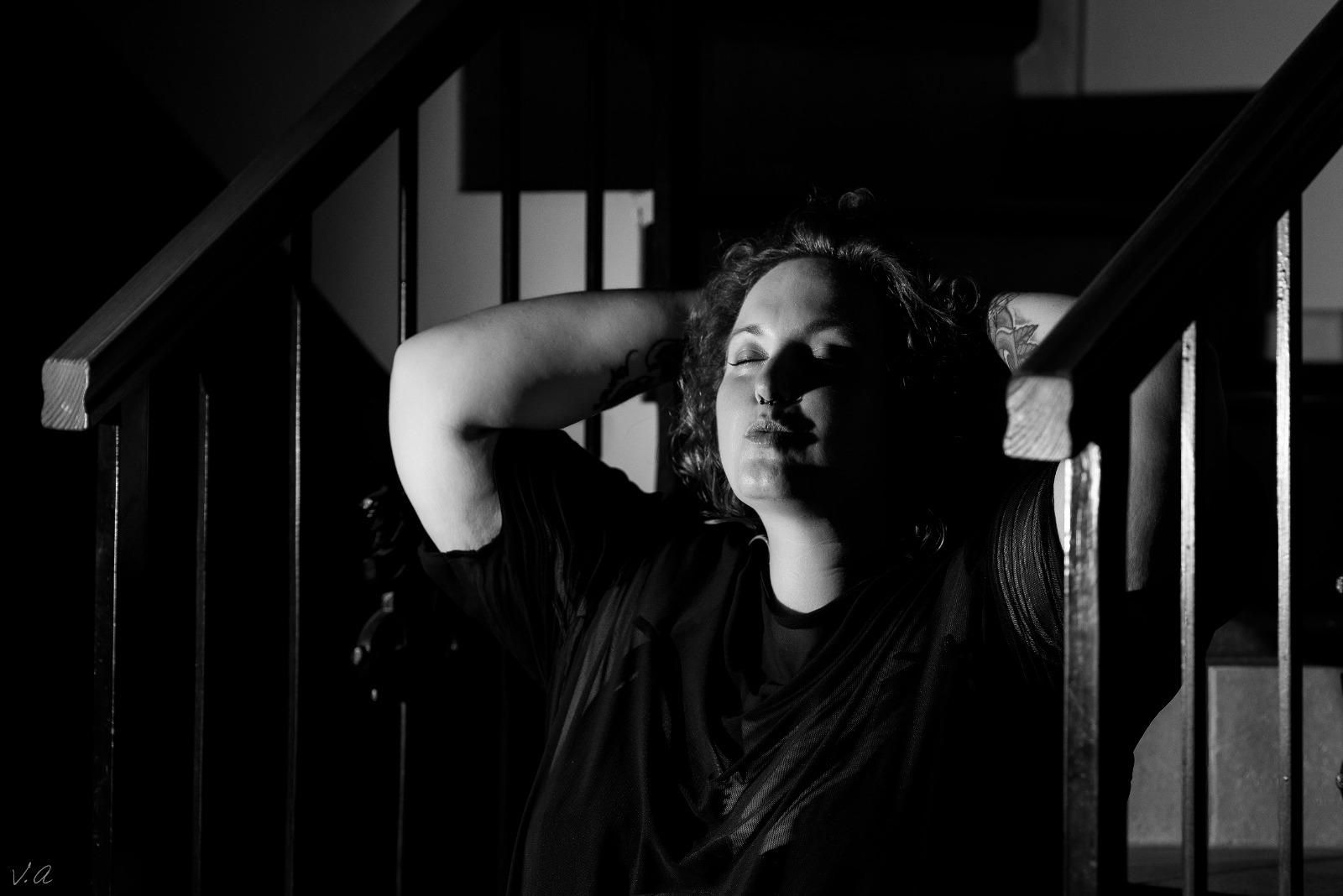 Mujer descansando en las escaleras, con las manos detrás de la cabeza, en la sombra.