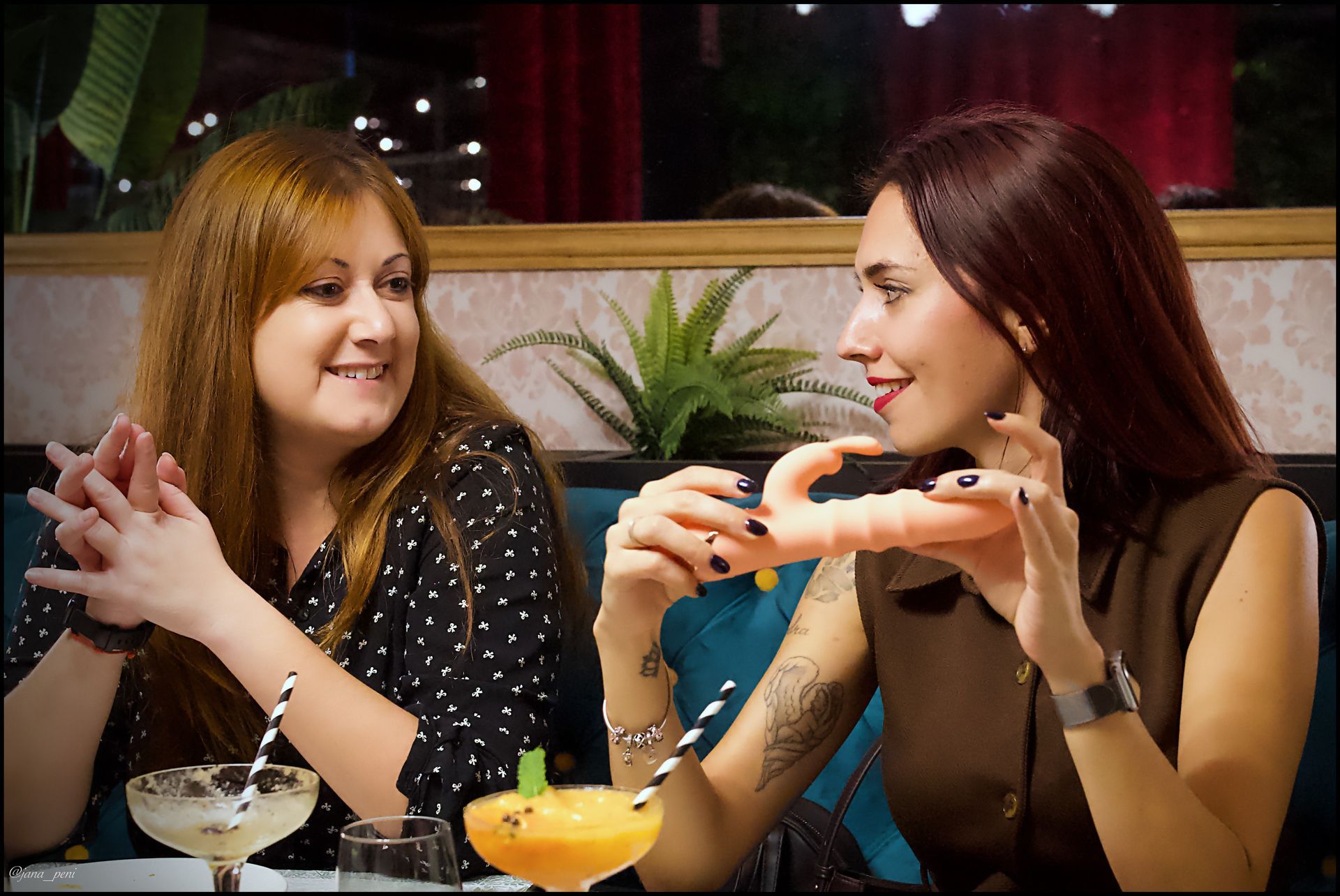 Dos mujeres sentadas a la mesa; una de ellas sostiene un objeto pequeño. Bebidas frente a ellas. Restaurante.