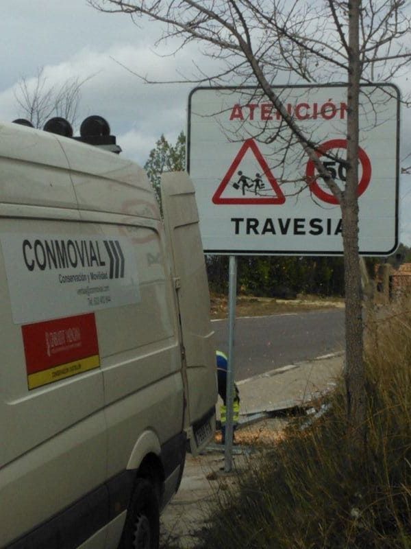 Furgoneta blanca estacionada cerca de una señal de tráfico que advierte de una zona escolar y un límite de velocidad de 50 km/h.