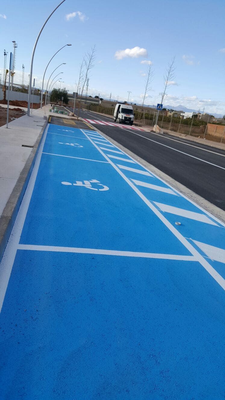 Espacios de estacionamiento para discapacitados pintados de azul en una calle, con una camioneta circulando por la carretera y farolas a lo largo de la acera.