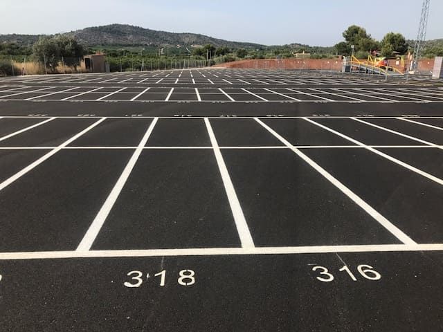 Estacionamiento vacío con espacios numerados y líneas blancas, con fondo rural.