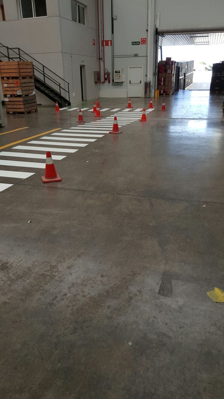 Almacén interior con paso de peatones pintado y conos de tráfico.