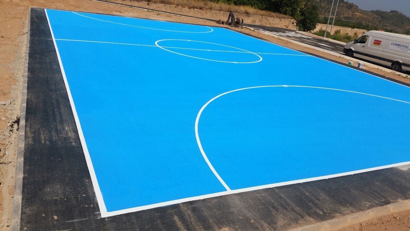 Cancha deportiva azul con líneas blancas, rodeada por un borde negro. La luz del sol ilumina el espacio exterior.
