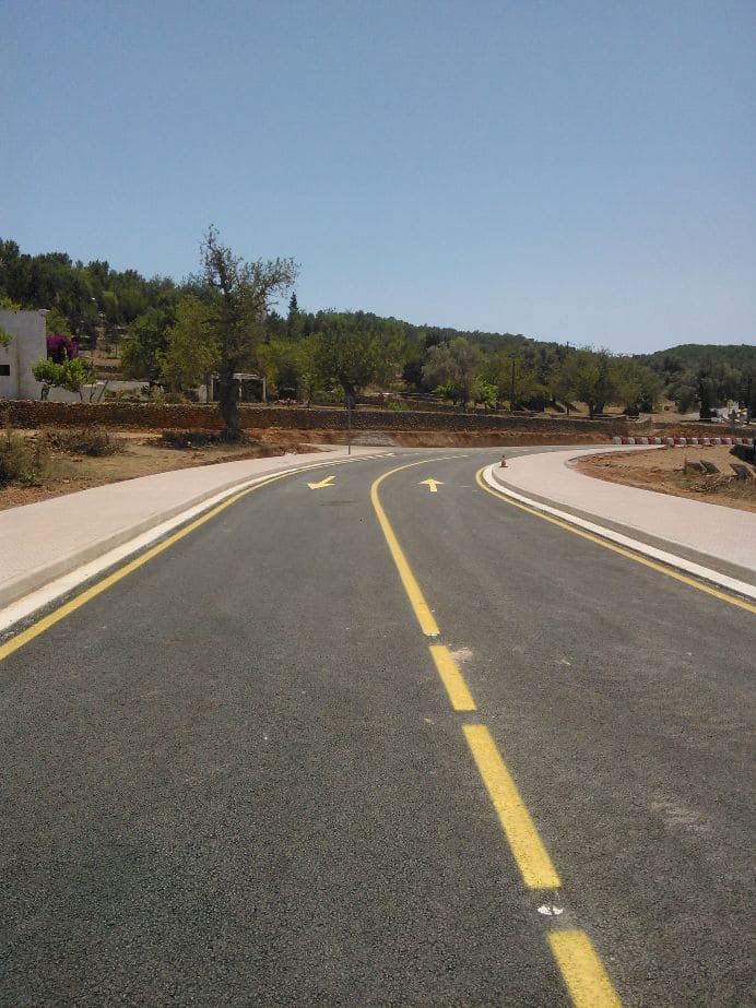 Carretera asfaltada con curvas, marcas amarillas en el carril, bordillo a ambos lados, día soleado.