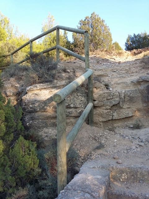 Barandilla de madera en un camino rocoso con vistas a un paisaje.