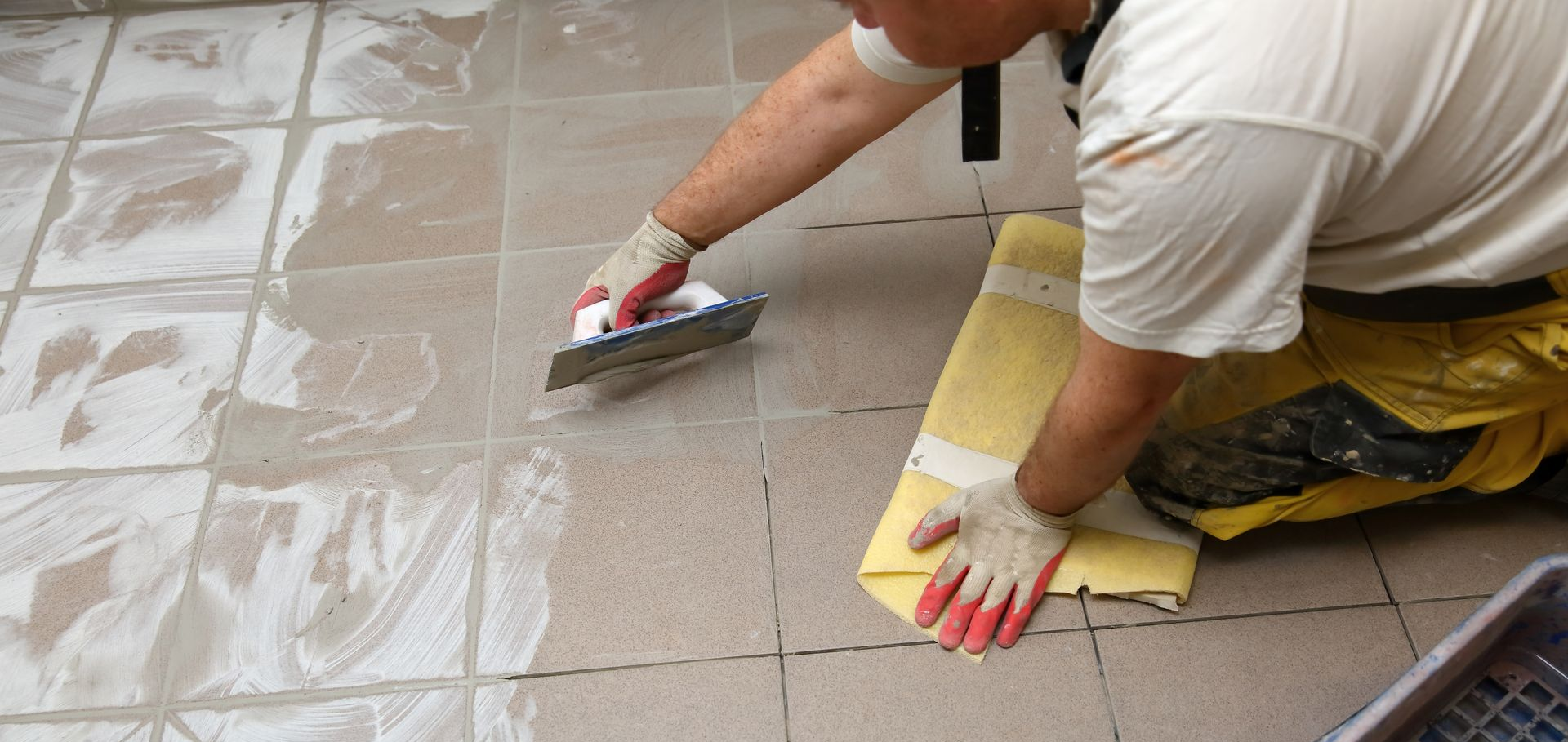 Une personne carrelant un sol, appliquant le joint à la truelle.