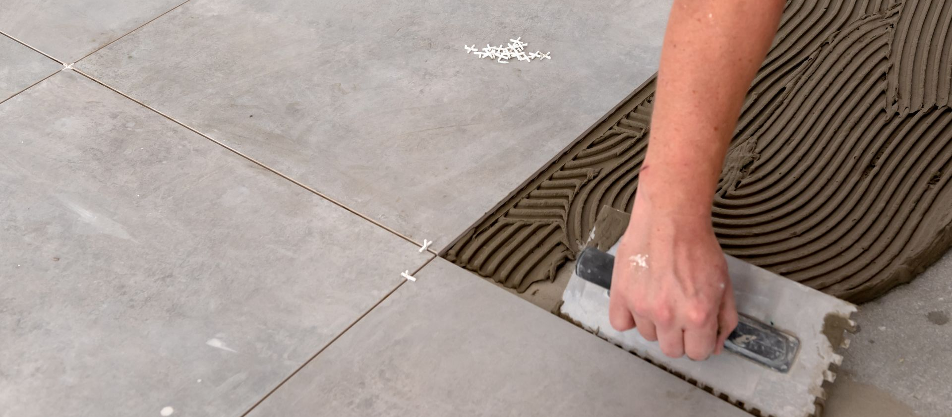 Une personne appliquant de la colle à carrelage à l'aide d'une truelle crantée sur un sol.