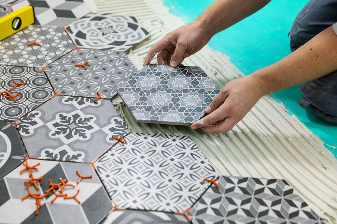Une personne pose des carreaux hexagonaux à motifs sur un sol, à l'aide de clips de nivellement orange.