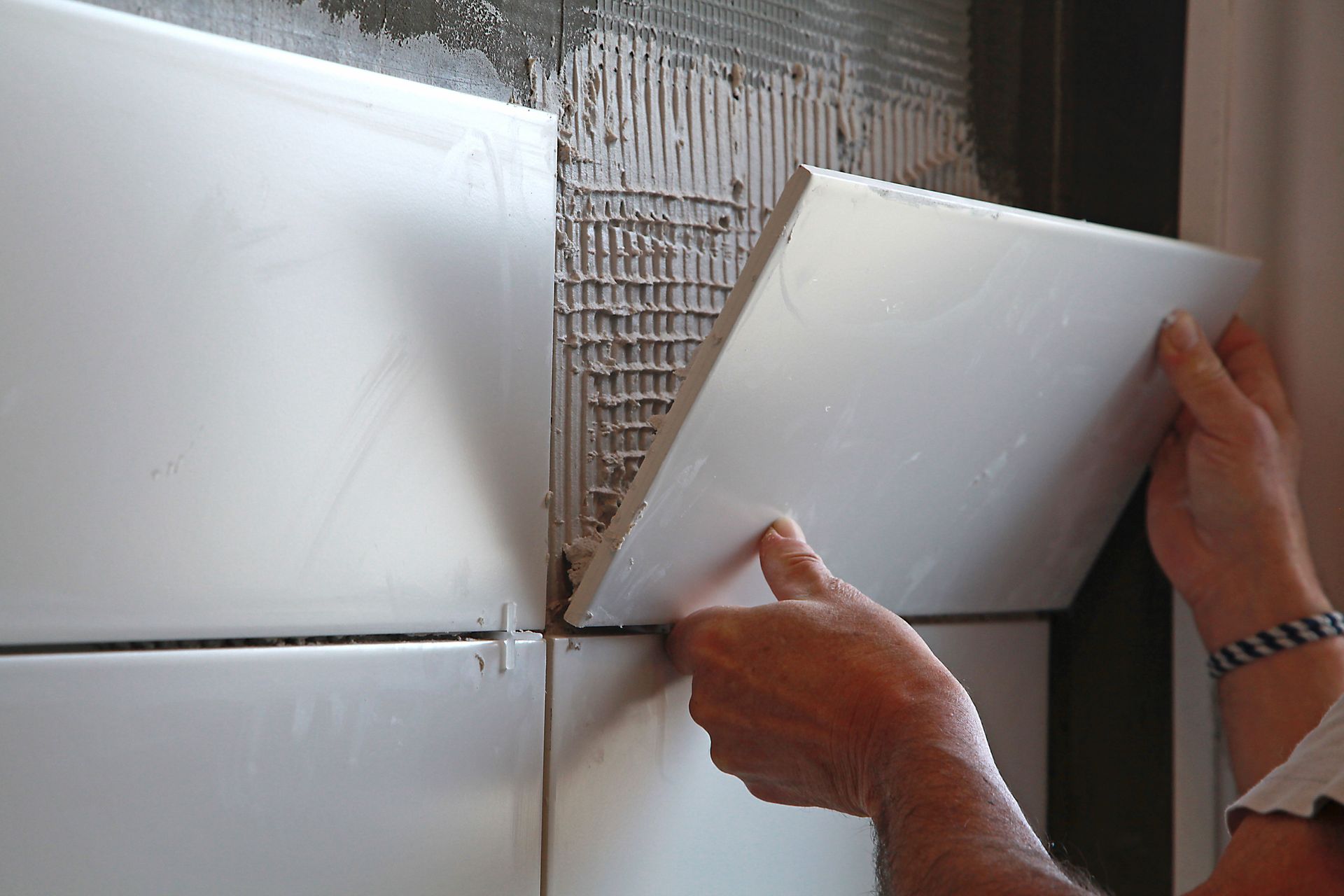 Personne posant des carreaux de céramique blancs sur un mur.