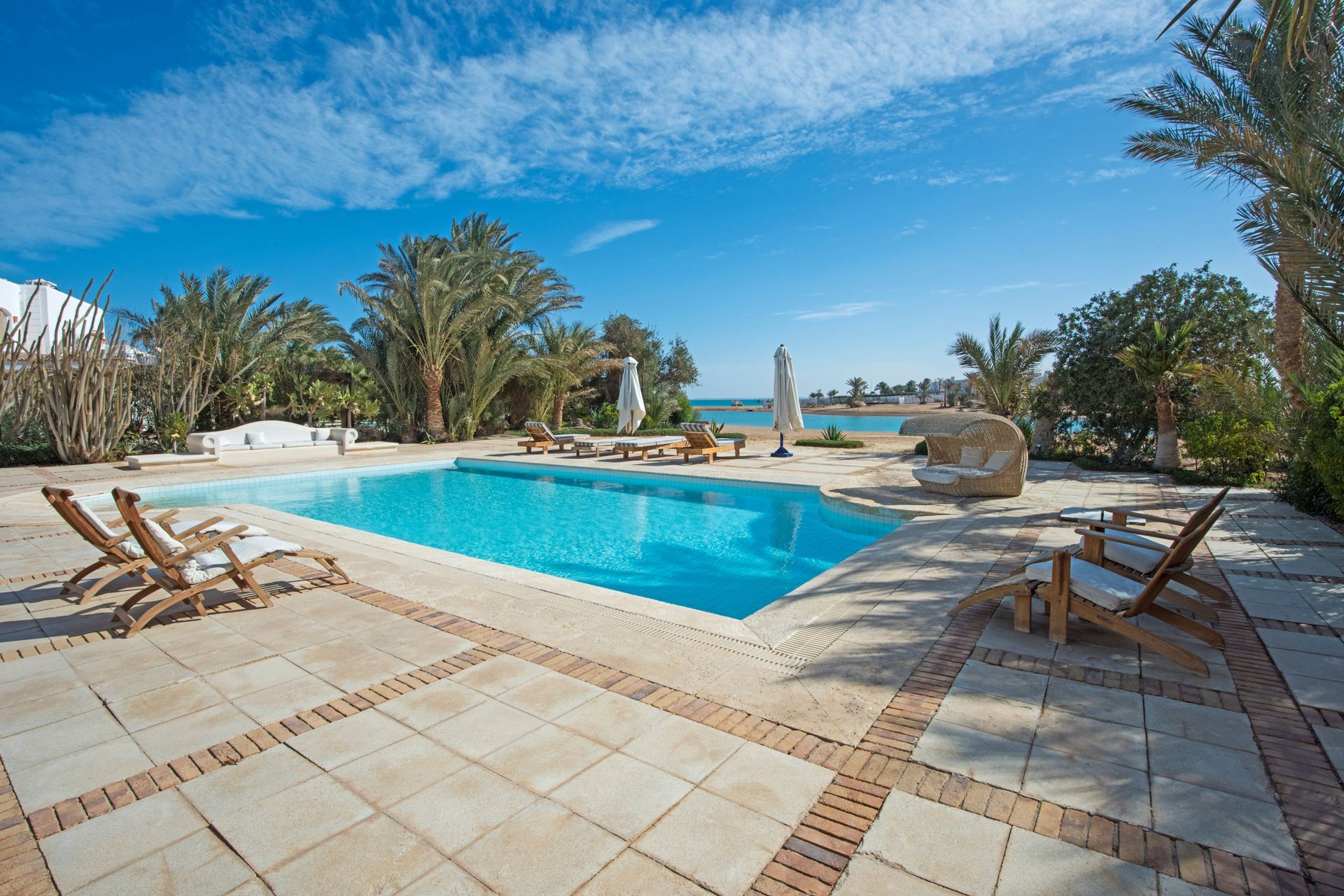 Une piscine bleue, avec des chaises longues et des arbres.