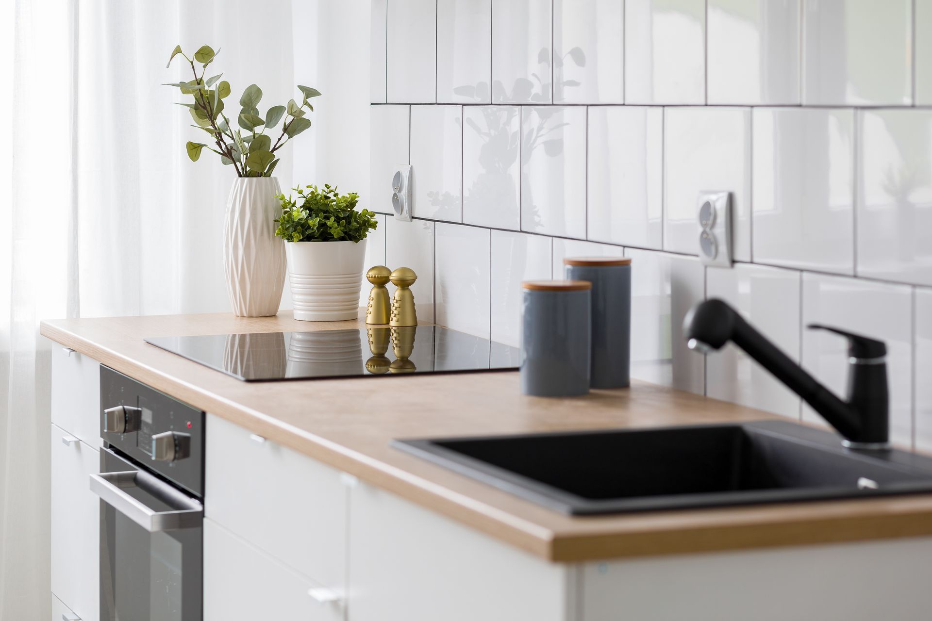 Cuisine moderne avec placards blancs, comptoir en bois clair, évier noir et éléments décoratifs.