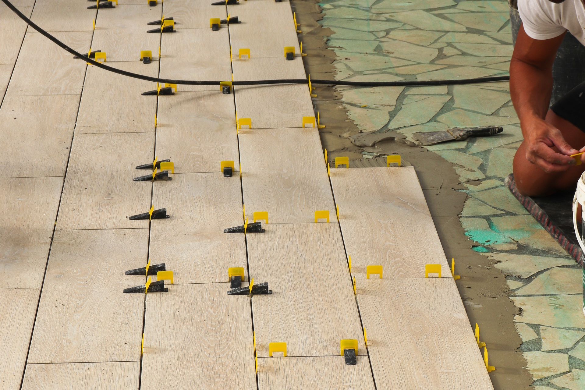 Pose de carrelage : des carreaux beiges sont posés avec des clips de nivellement jaunes.