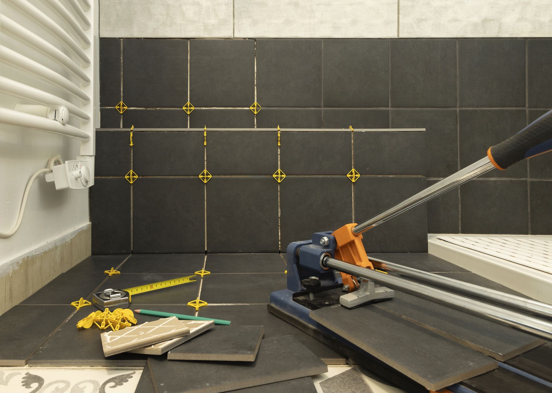 Pose de carrelage mural dans la salle de bains à l'aide d'une carrelette. Les carreaux foncés sont posés avec des croisillons et un niveau.