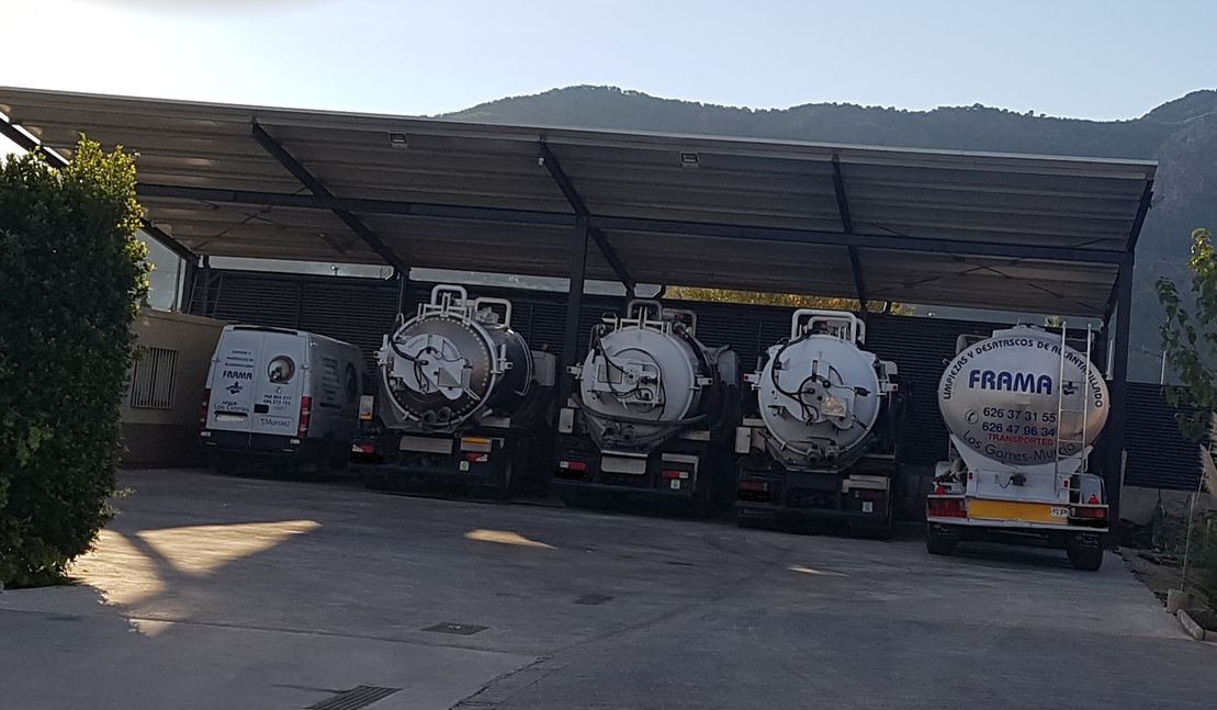 Una fila de camiones blancos están estacionados bajo un toldo en un estacionamiento.