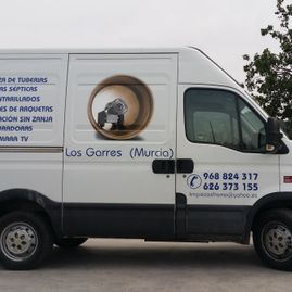 Una camioneta blanca con un dibujo de una tubería en el costado está estacionada al costado de la carretera.