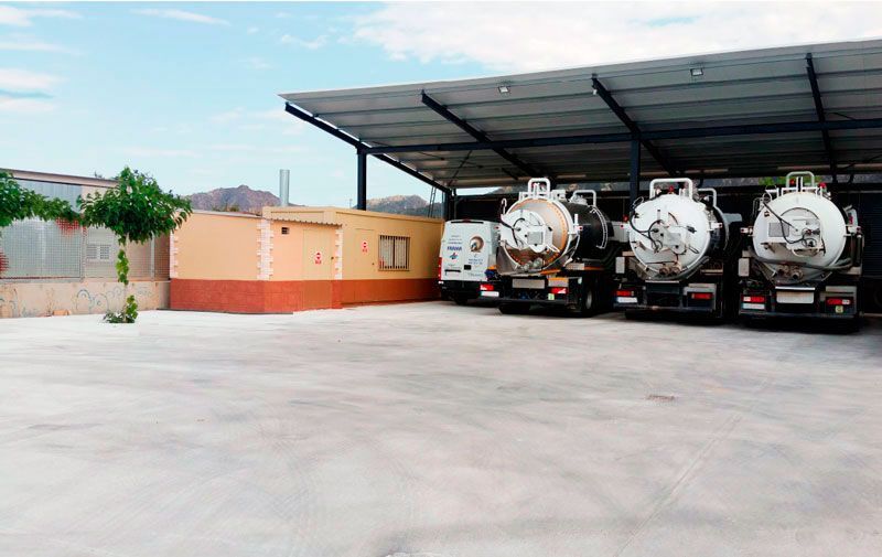 Una fila de camiones están estacionados bajo un techo en un estacionamiento.