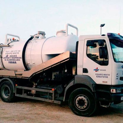 Un camión blanco con un gran tanque en la parte trasera está estacionado en la tierra.