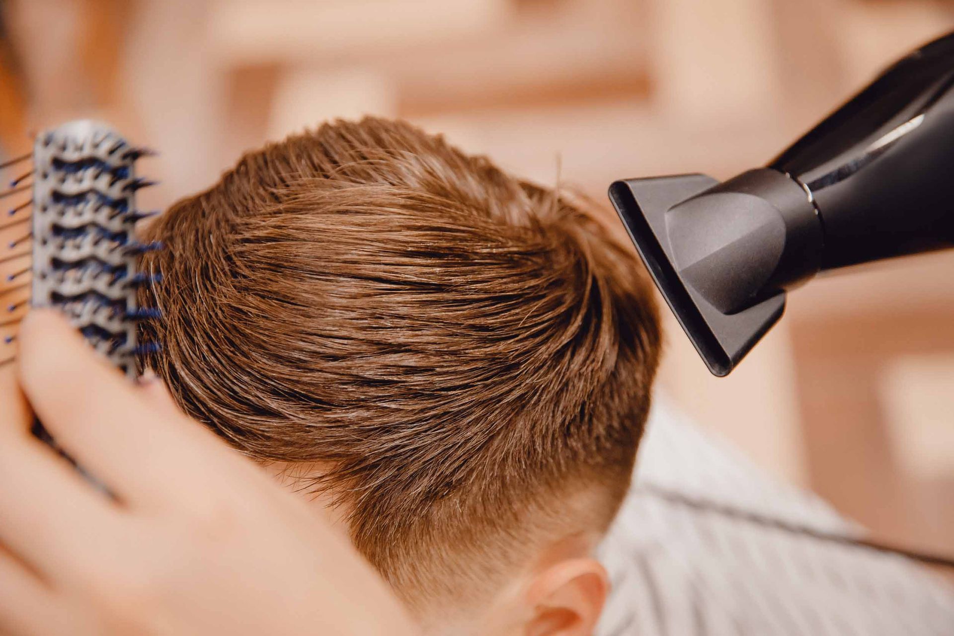 Un peluquero seca el cabello de una clienta con un secador y un cepillo negros en un salón.
