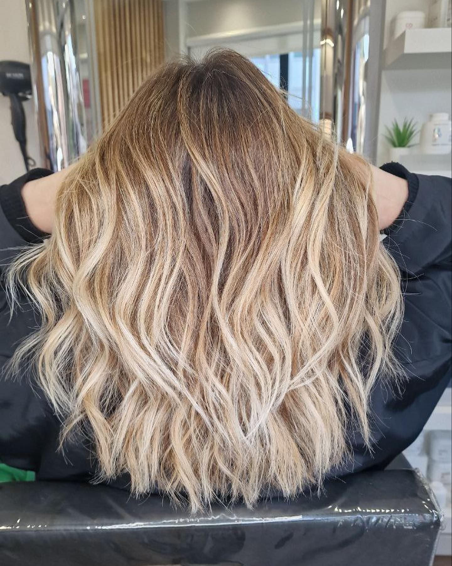 Ondas balayage rubias, raíces marrones, manos en la cabeza, en el salón.