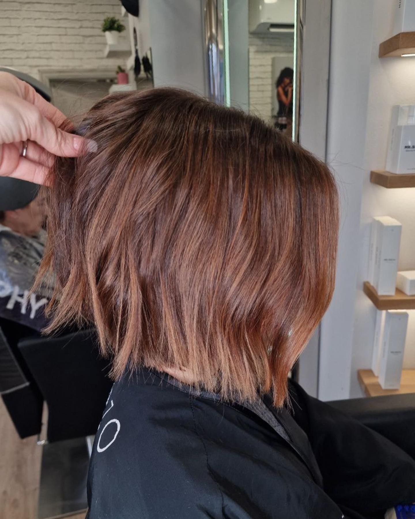 Mujer con cabello castaño rojizo en capas siendo peinada en una peluquería. Su mano levanta mechones para mostrar el corte y el color.