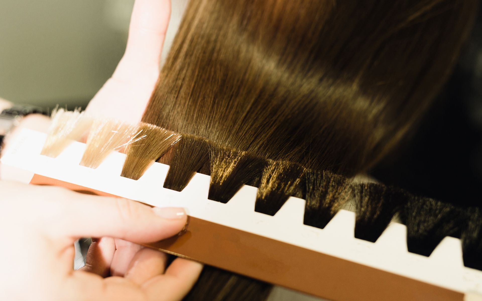 Mano sosteniendo una guía de muestras de color de cabello junto a mechones de cabello castaño para comparar tonos.