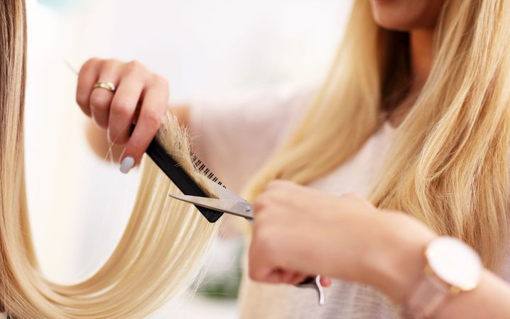 Manos con guantes negros mezclando tinte para el cabello morado en un recipiente negro sobre un fondo blanco.