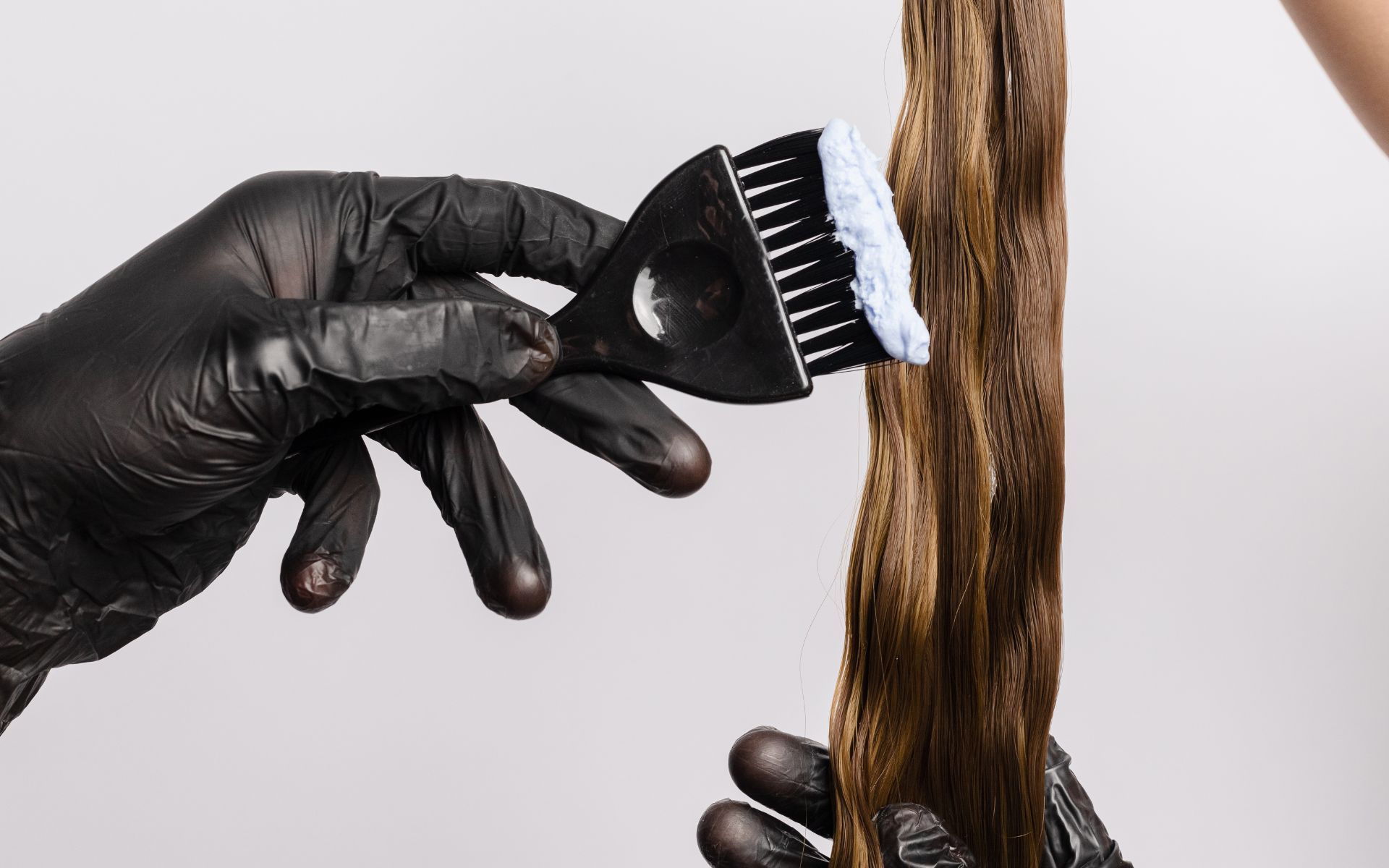 Persona que usa guantes negros aplica tinte para el cabello en mechones de cabello castaño con un cepillo negro.