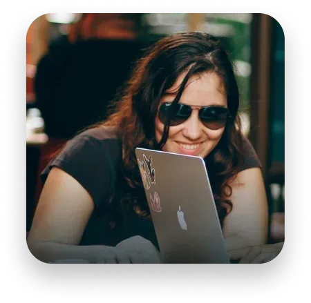 Woman wearing sunglasses smiles while looking at a laptop.