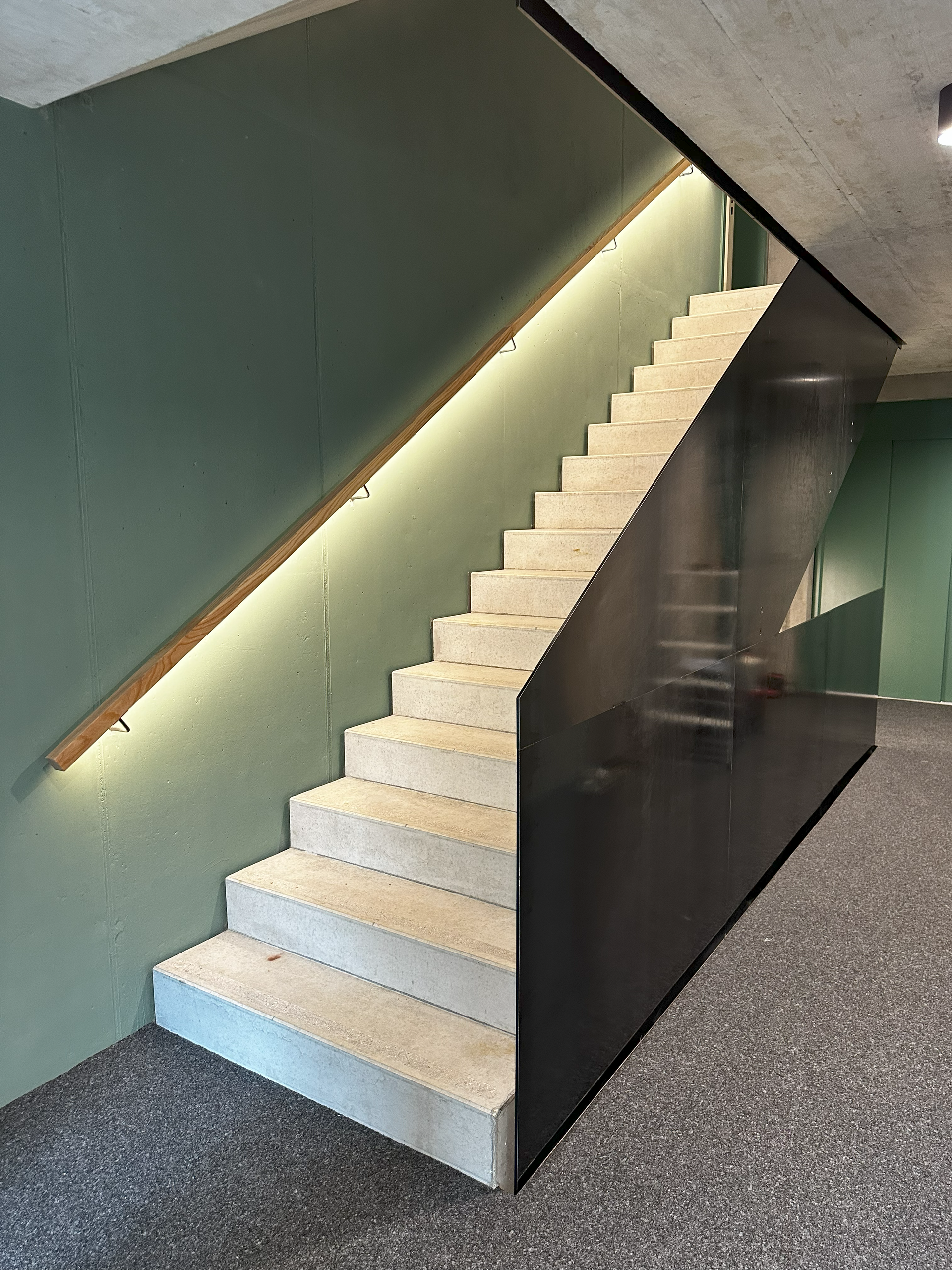 Vor einer grauen Wand steht eine Wendeltreppe aus Metall.