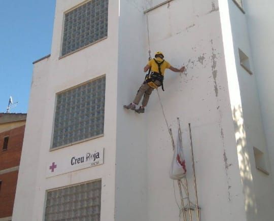 Un hombre con una camisa amarilla está subiendo por el costado de un edificio blanco.