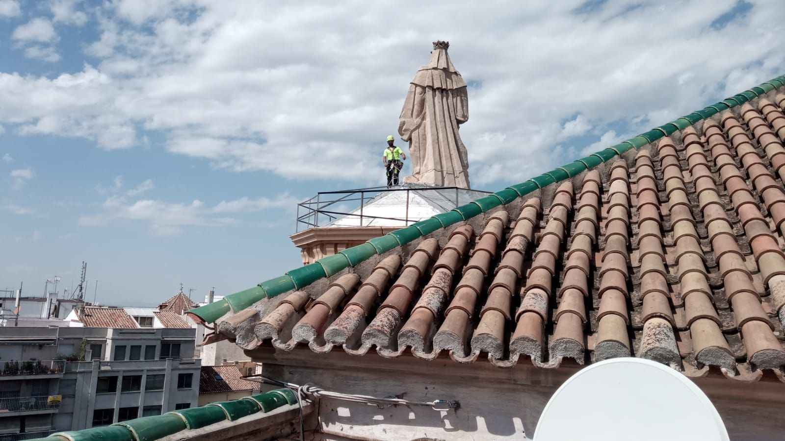 Un hombre está de pie sobre un tejado con una estatua al fondo.
