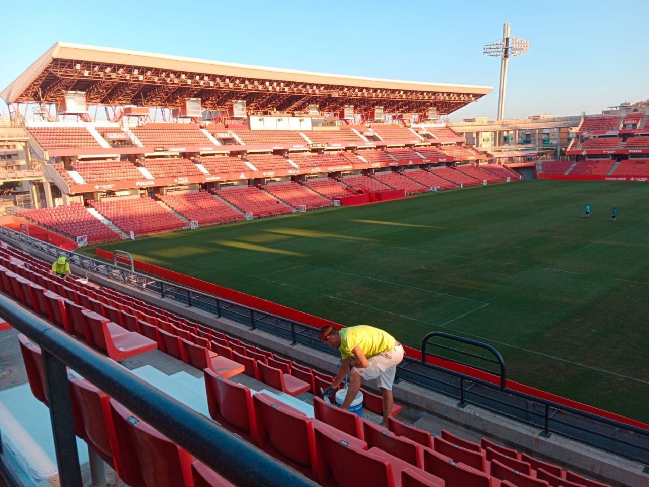 Un hombre con una camiseta amarilla está limpiando los asientos de un estadio.
