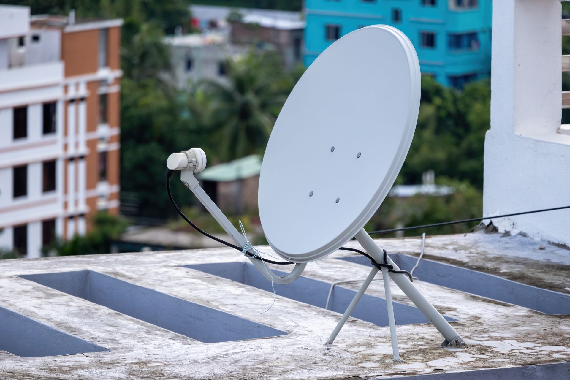 Antenne parabolique blanche sur un toit, avec des bâtiments en arrière-plan.