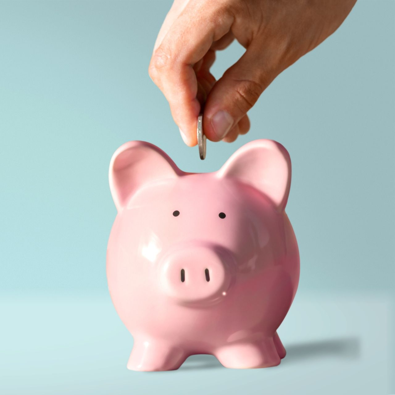 Une main déposant une pièce dans une tirelire.