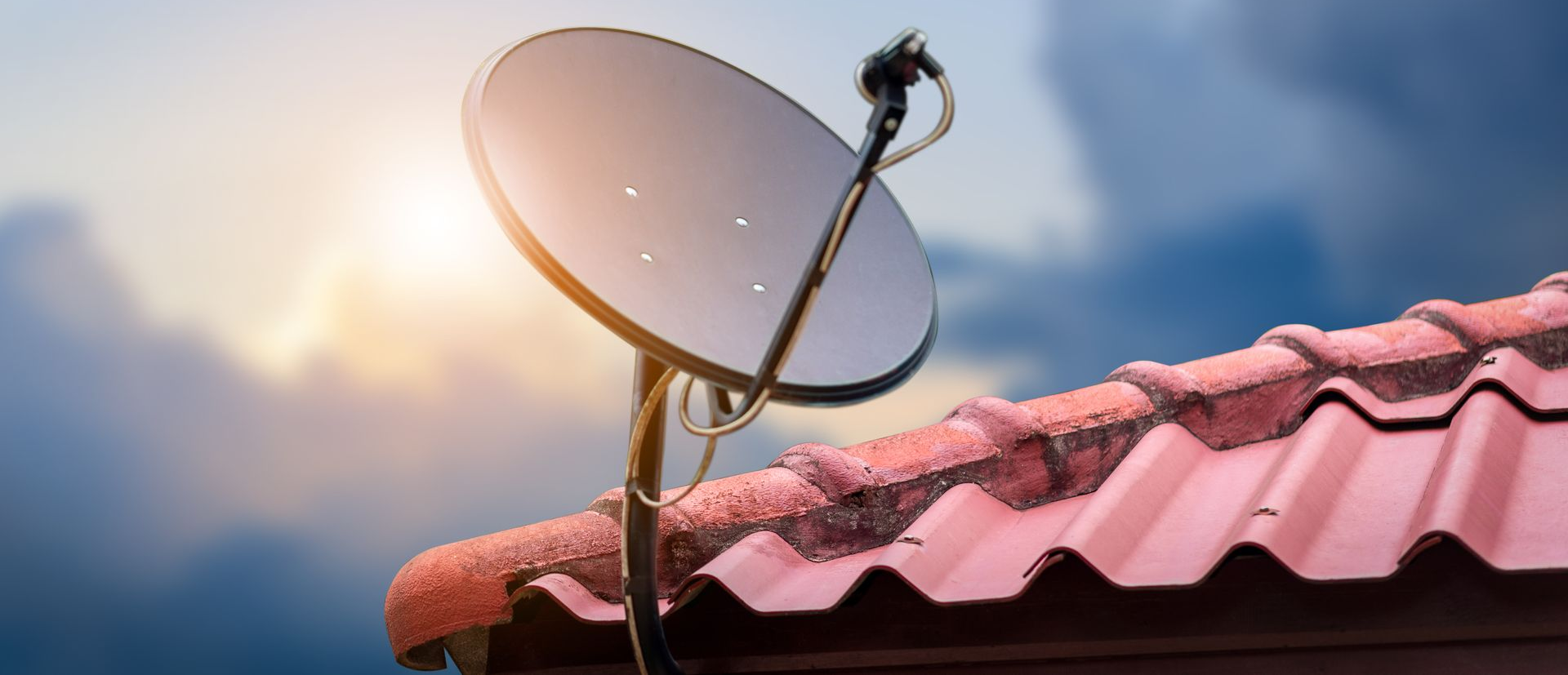 Antenne parabolique fixée sur un toit de tuiles rouge.