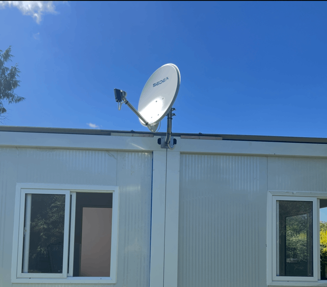 Antenne parabolique fixée sur un bâtiment blanc avec des fenêtres.