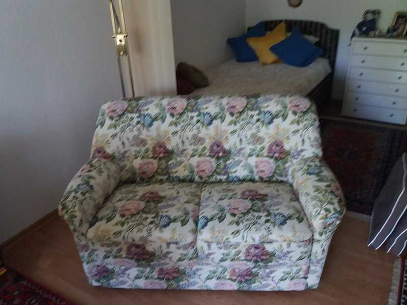Eine geblümte Couch steht in einem Zimmer neben einem Bett