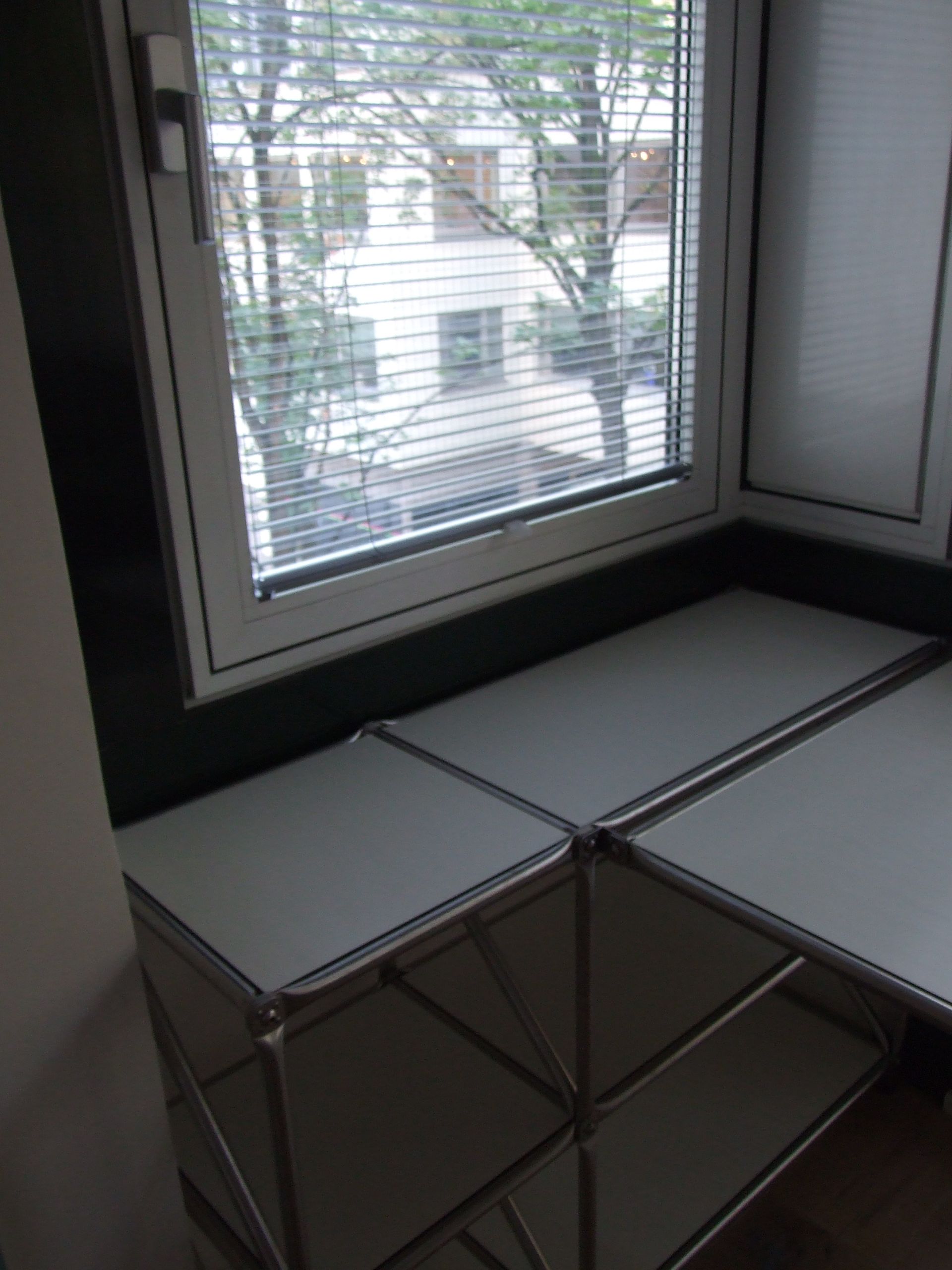 Es gibt ein Fenster mit Jalousien und einem Tisch davor.