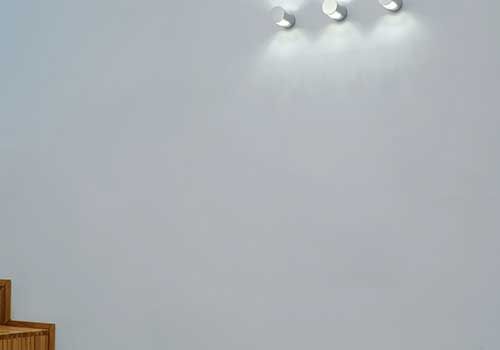 Eine weiße Wand mit drei Lichtern darauf und einem Holzstuhl.