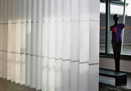 Eine Schaufensterpuppe steht vor einem Fenster neben einer Reihe weißer Vertikaljalousien.