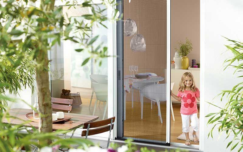 Ein kleines Mädchen steht vor einer Glasschiebetür.