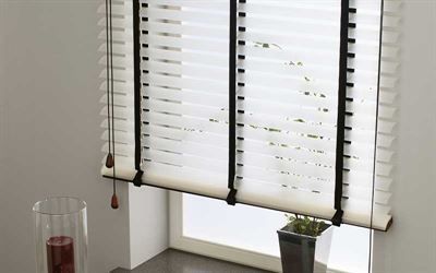 Eine weiße Jalousie hängt an einem Fenster neben einer Vase mit Blumen.