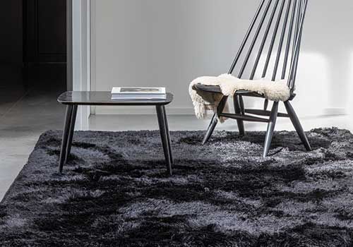 Ein Stuhl steht auf einem schwarzen Teppich neben einem Couchtisch.