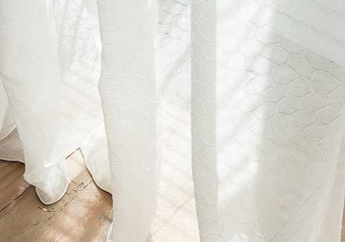 Eine Nahaufnahme eines Paars weißer Vorhänge an einem Fenster.