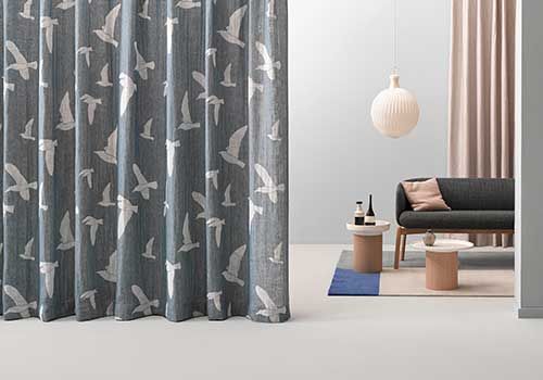 Ein Wohnzimmer mit einer Couch, Tischen und Vorhängen mit Vögeln darauf.