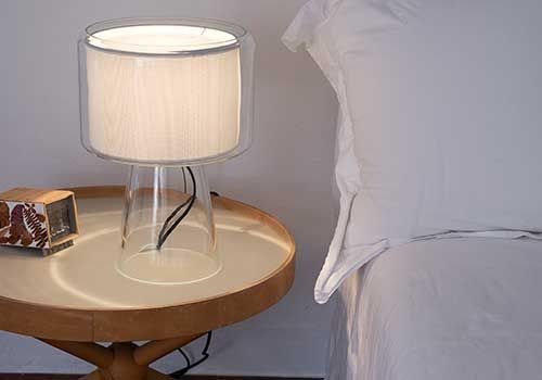 Auf einem Holztisch neben einem Bett steht eine Lampe.