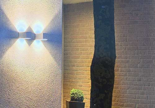 Eine Backsteinmauer mit zwei Lichtern darauf und einem Baum im Hintergrund.