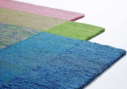 Drei verschiedenfarbige Teppiche liegen übereinander auf einer weißen Fläche.