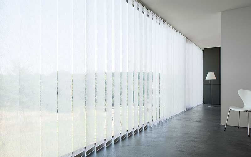 Ein Zimmer mit weißen Vertikaljalousien an den Fenstern
